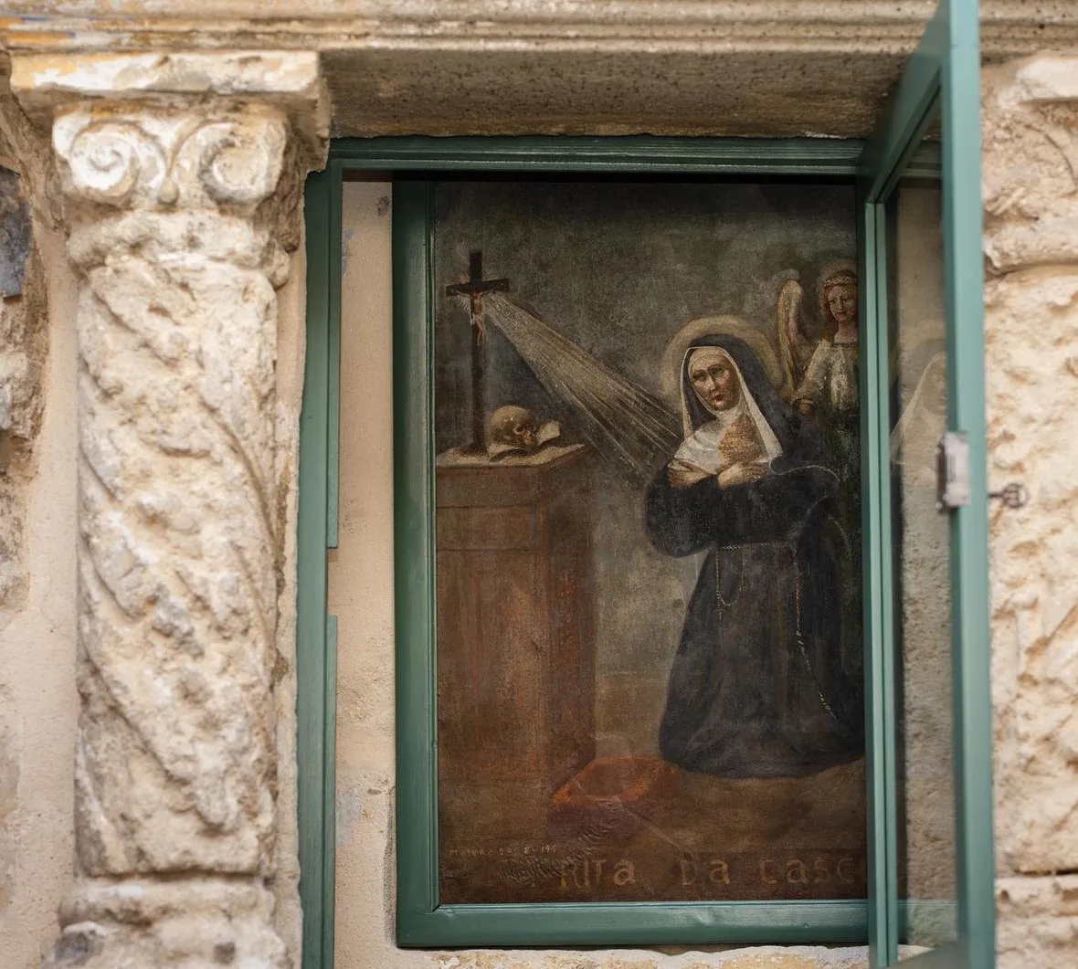 Dipinto devozionale in una cornice verde, tra elementi in pietra